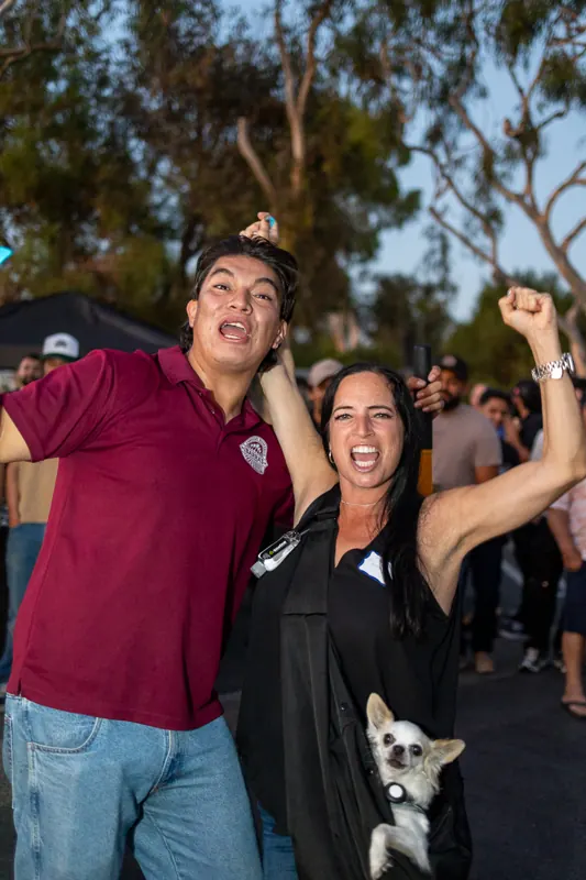 A man and a woman cheering during the raffle, the woman holding a chihuahua.
